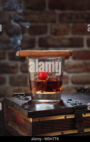 Glass of whiskey with smoking cigar and ice cubes on wooden table. Stock Photo