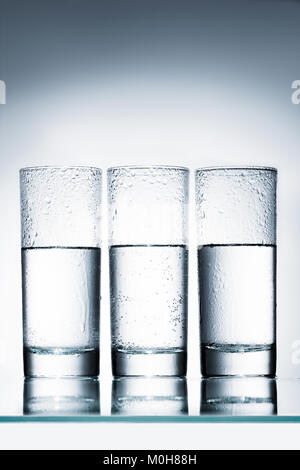 half full glasses of water in row on reflective surface Stock Photo