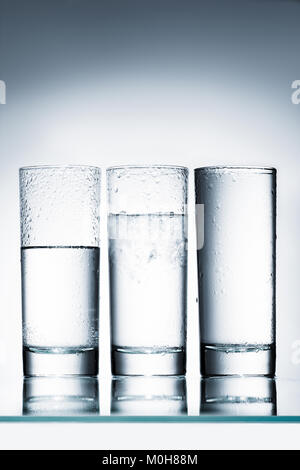 glasses of water in row of different levels on reflective surface Stock Photo