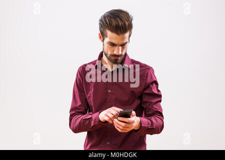 Studio shot portrait of young businessman who is typing on mobile phone. Stock Photo