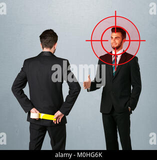 Ruthless businessman handshake with a hiding weapon and a head target point Stock Photo