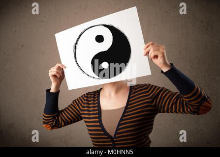 Young woman holding a paper with a yin-yang symbol on it in front of her head Stock Photo