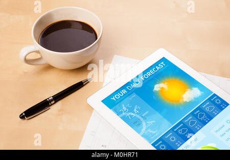 Workplace with tablet pc showing weather forecast and a cup of coffee on a wooden work table close-up Stock Photo