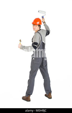A young man in working grey clothes and orange hard helmet painting the walls in the room. Stock Photo