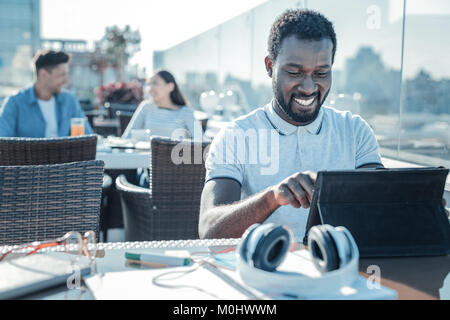 Happy african american grinning broadly while using touchpad Stock Photo