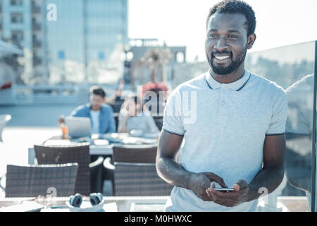 Pensive african american guy with smartphone dreaming and smiling Stock Photo
