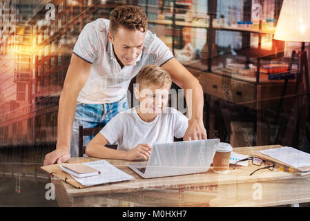 Attentive father pointing to the screen while helping his son with homework Stock Photo
