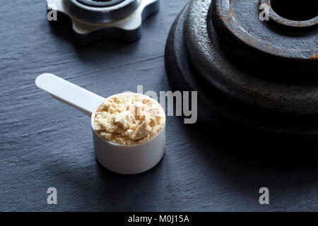 Measuring scoop filled with protein powder and weight plates on dark background Stock Photo