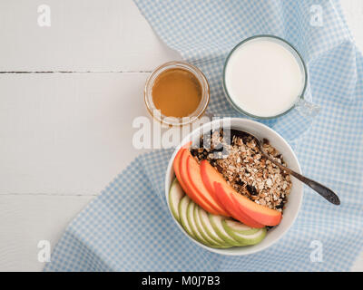 Healthy and tasty breakfast - muesli, slices of persimmon and apple, a glass of fresh milk and maple syrup in a cup on a white table top Stock Photo