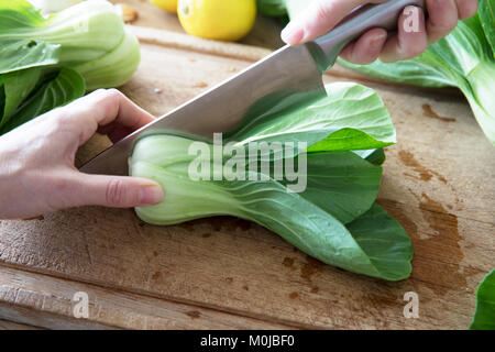 Slicing boy choi in half  with chef's knife on cutting board. Stock Photo