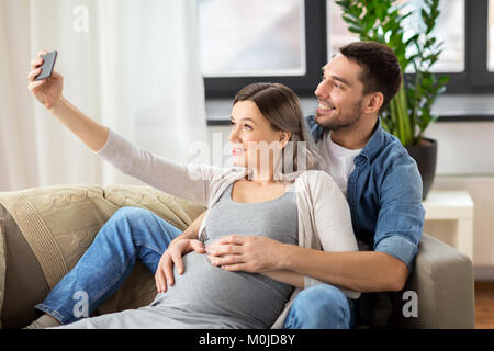 man and pregnant woman taking selfie at home Stock Photo