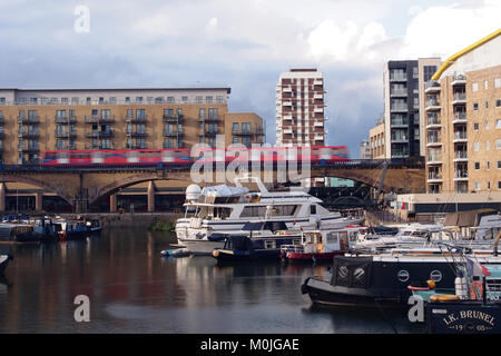 A view of barges and boats at Limehouse basin, east London with residential properties in the background and a DLR train passing through on a bridge Stock Photo