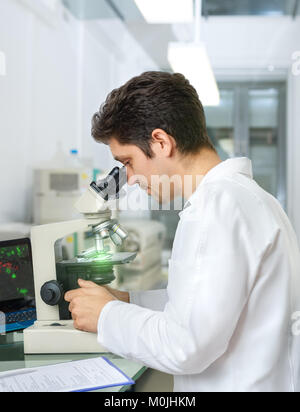 Male scientist or tech with dark hair and brown eyes works with microscope samples in research facility Stock Photo