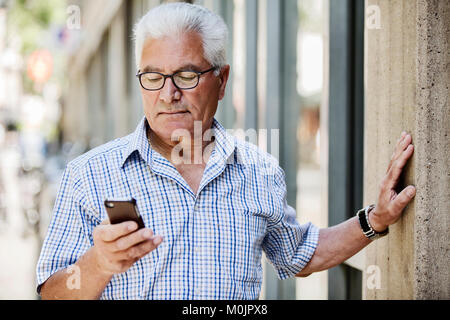 Grey-haired Senior with glasses and smartphone in the city, Cologne, North Rhine-Westphalia, Germany Stock Photo