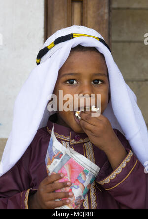 Young boy in traditional suit dressed for the Mawlid festival, eating popcorn, Lamu Island, Kenya Stock Photo