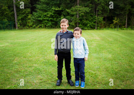 Two boys standing on lawn with hand on each shoulder dressed in formalwear -smiling, making fun, brothers portrait, togetherness, mischievous, bonding