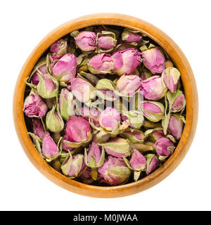 Dried rose buds in wooden bowl. Flowering plant of the genus Rosa. Used as decoration, as scent, for teas and perfums. Isolated macro food photo. Stock Photo