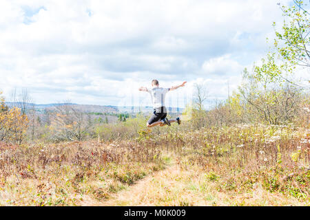 Young athletic, fit, free happy man running jogging jumping in autumn, fall, summer meadow field path hike in mid-air, muscles Stock Photo