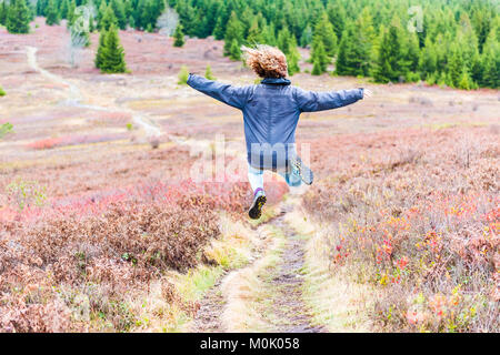 Young athletic, fit, free happy woman running jogging jumping in autumn, fall season meadow field path hike in mid-air Stock Photo