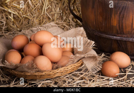 Brown chicken eggs in a basket and on a straw covered wooden surface Stock Photo