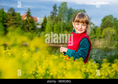Little girl walking outdoors in the summer meadow with yellow flowers (Barbarea vulgaris, Winter Cress, Common Winter-cress, Yellow Rocket, Stock Photo