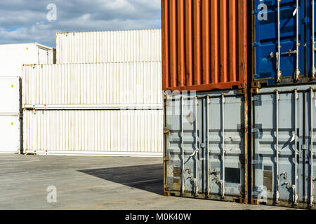 Worn intermodal containers stacked in a shipping yard with newer white pallet wide and refrigerated containers in the background. Stock Photo