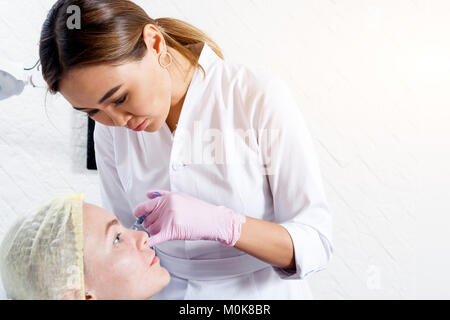 Close-up Young woman doctor cosmetician in white lab coat and sterile gloves makes Botox injection with syringe Stock Photo