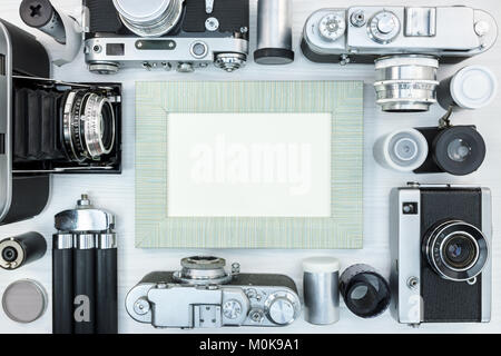 old classic photo cameras, empty photo frame, negative film rolls and tripod on white wooden background top view Stock Photo