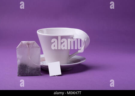 Empty porcelain white cup with single teabag on purple background. studio shot Stock Photo