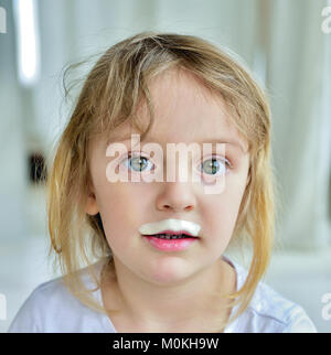 Close up fun portrait of cute  little girl with milk moustaches. Portrait of a little happy girl with yogurt on the face. Stock Photo