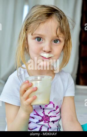 Close up fun portrait of cute  little girl with milk moustaches. Portrait of a little happy girl with yogurt on the face. Stock Photo