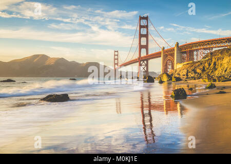 Classic panoramic view of famous Golden Gate Bridge seen from scenic Baker Beach in beautiful golden evening light on a sunny day with blue sky and cl Stock Photo