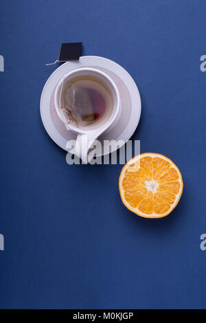 Porcelain white cup tea with sliced orange on dark blue background. top view studio shot Stock Photo