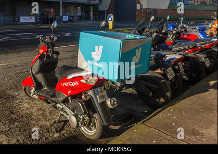 Deliveroo food box on the back of a parked motor scooter on the side of the road in Cork, Ireland. Stock Photo