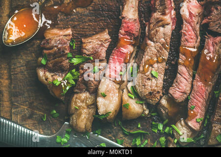 Flat-lay of grilled medium rare ribeye beef steak cut into peices on rustic wooden board with mango chutney sauce, horizontal composition Stock Photo