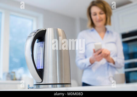 Woman Controlling Smart Kettle Using App On Mobile Phone Stock Photo