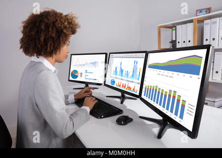 Businesswoman Analyzing Graph On Multiple Computers On Desk In Office Stock Photo