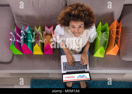 Happy Young Woman Using Laptop With Multi Colored Shopping Bags On Carpet Stock Photo