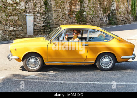 Young man driving yellow vintage Fiat 850 Sport Coupe released circa 1970 in Italy. Stock Photo