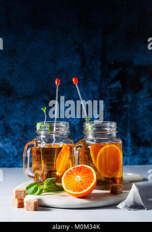 Traditional iced tea with orange and mint and ice in mason jars . refreshing summer drink on white marble board Stock Photo