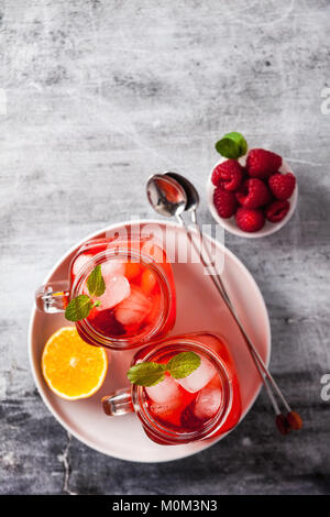 summer refreshing drink with ice and fresh ripe berries. raspberries and blackberries with citrus on a stone background table in glass jars with handl Stock Photo