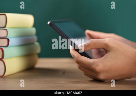Close-up Of A Student's Hand Using Digital Tablet With Stacked Books On Desk Stock Photo