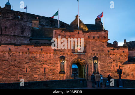 Edinburgh Castle entrance and esplanade lit up at dusk, Edinburgh, Scotland, UK with tourists and staff member Stock Photo