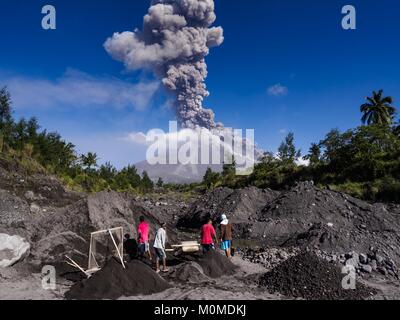 Daraga, Albay, Philippines. 23rd Jan, 2018. Sand and gravel miners work in a riverbed of volcanic soil while the Mayon volcano erupts Tuesday. The Mayon volcano continued to erupt Tuesday, although it was not as active as it was Monday. There were ash falls in communities near the volcano. This is the most active the volcano has been since 2009. Schools in the vicinity of the volcano have been closed and people living in areas affected by ash falls are encouraged to stay indoors, wear a mask and not participate in strenuous activities. Credit: Jack Kurtz/ZUMA Wire/Alamy Live News Stock Photo