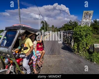 Daraga, Albay, Philippines. 23rd Jan, 2018. People leave a community close to the Mayon volcano as smoke from an eruption builds over the volcano. The Mayon volcano continued to erupt Tuesday, although it was not as active as it was Monday. There were ash falls in communities near the volcano. This is the most active the volcano has been since 2009. Schools in the vicinity of the volcano have been closed and people living in areas affected by ash falls are encouraged to stay indoors, wear a mask and not participate in strenuous activities. Credit: Jack Kurtz/ZUMA Wire/Alamy Live News Stock Photo