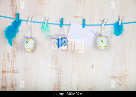 Easter Eggs,feathers and paper on a rope on a blue wooden background.  Easter still life can be used as a postcard. Stock Photo