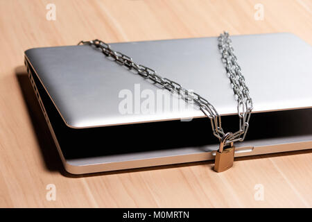 Heavy chain with a padlock around a laptop on table. Stock Photo