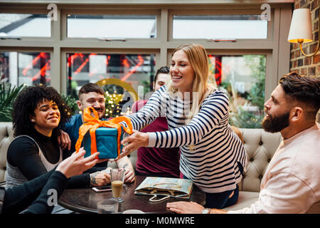 Friends are hanging out in a bar, celebrating one of the women's birthday. She is leaning over the table to receive a gift. Stock Photo