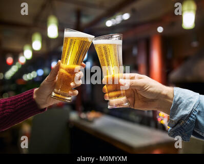 Beer glasses raised in a toast. Close-up hands with glasses. Blurred bar interior at the background. Stock Photo