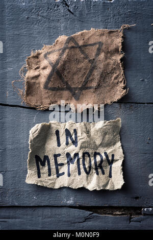 high angle view of a ragged jewish badge and a yellowish piece of paper with the text in memory written in it, on a gray rustic wooden surface Stock Photo